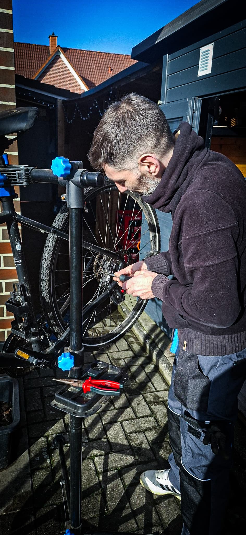 Bärtiger Mann repariert die Gangschaltung eines Fahrrads in einem Montageständer an einem sonnigen Tag.