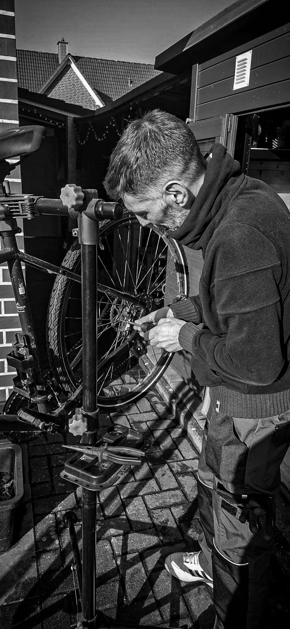 Ein bärtiger Mann repariert mit einem Schraubenzieher die Gangschaltung eines Fahrrads am Montageständer.